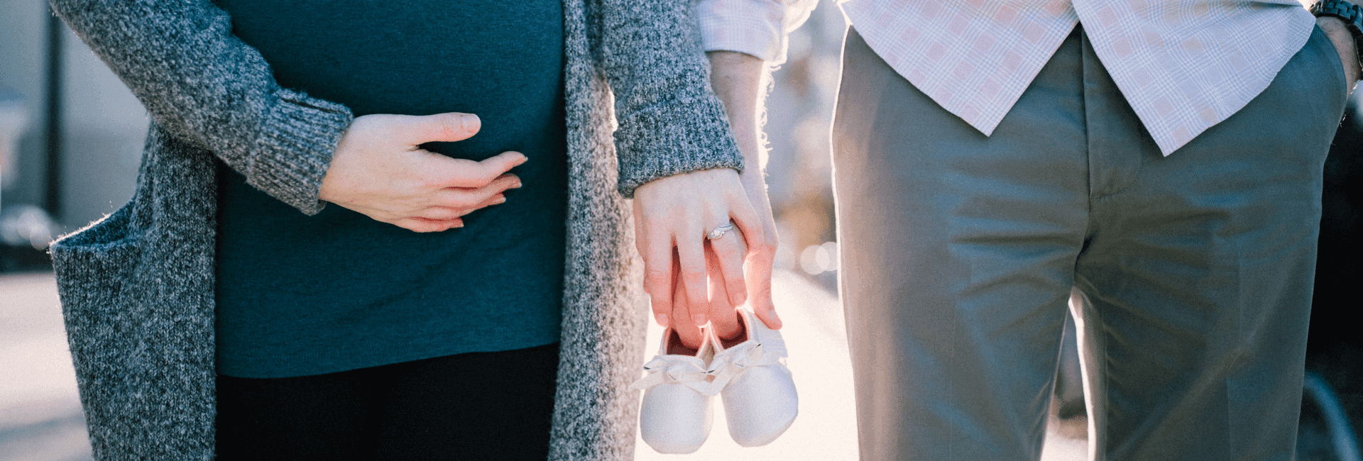 futurs parents avec maman enceinte et papa qui tiennent des chaussons de bébé